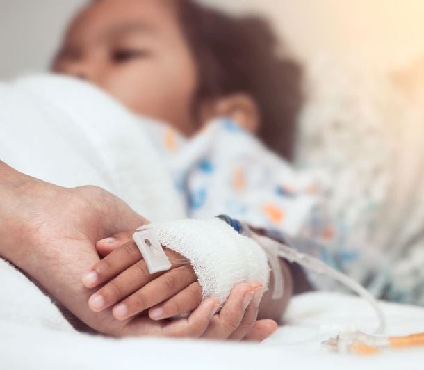 Young boy in hospital bed holds and adult's hand