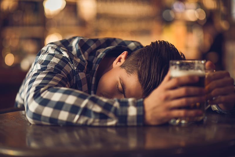 man slumped on counter with beer in hands