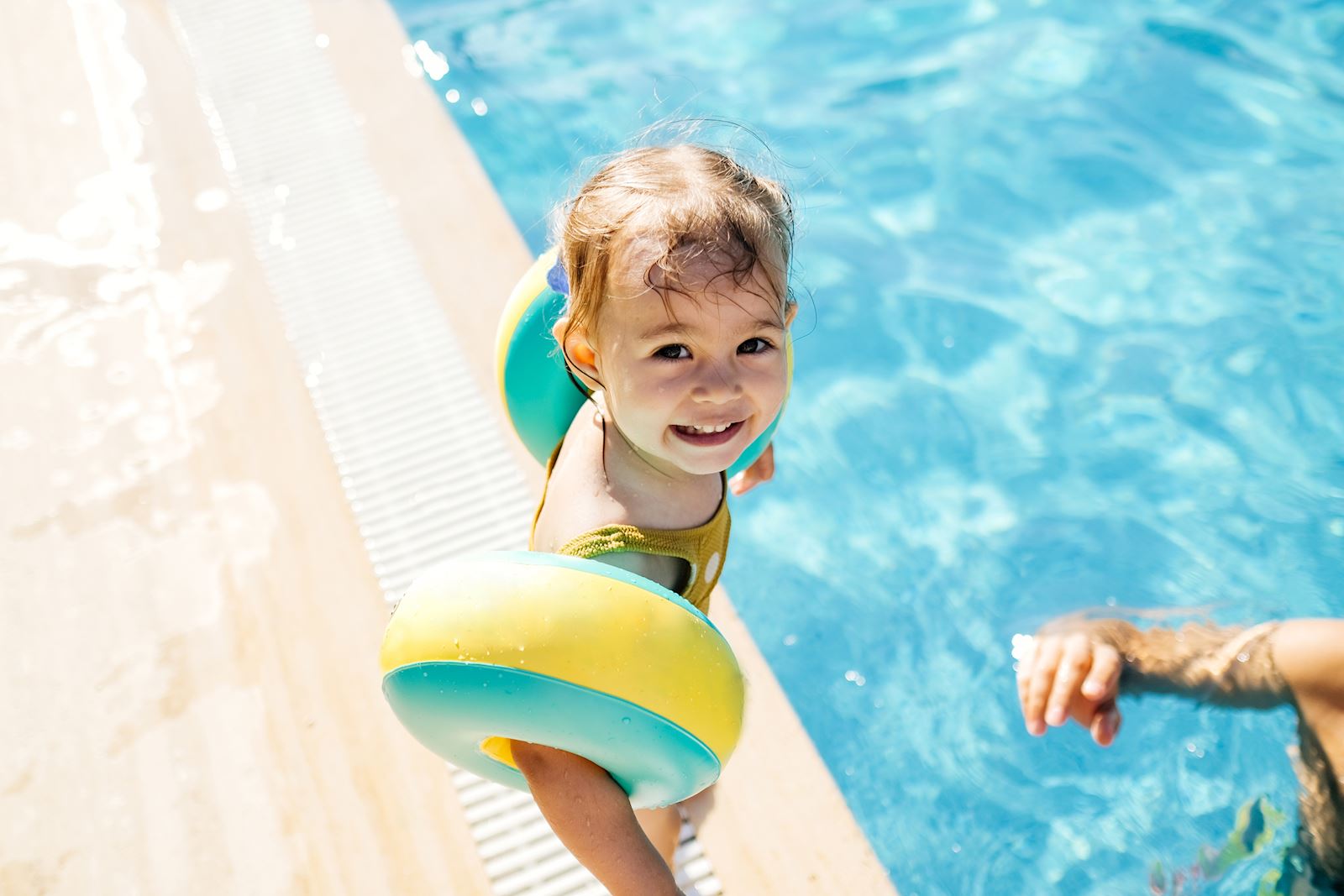 small child with arm flotation devices standing outside a pool