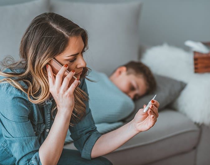 woman on phone looking at thermometer while boy sleeps behind her