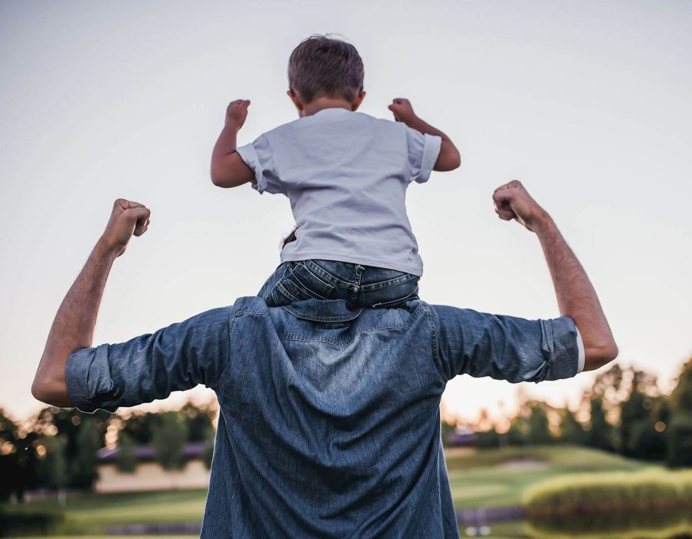 boy sits on dad's shoulders, both making a flexing pose with their arms