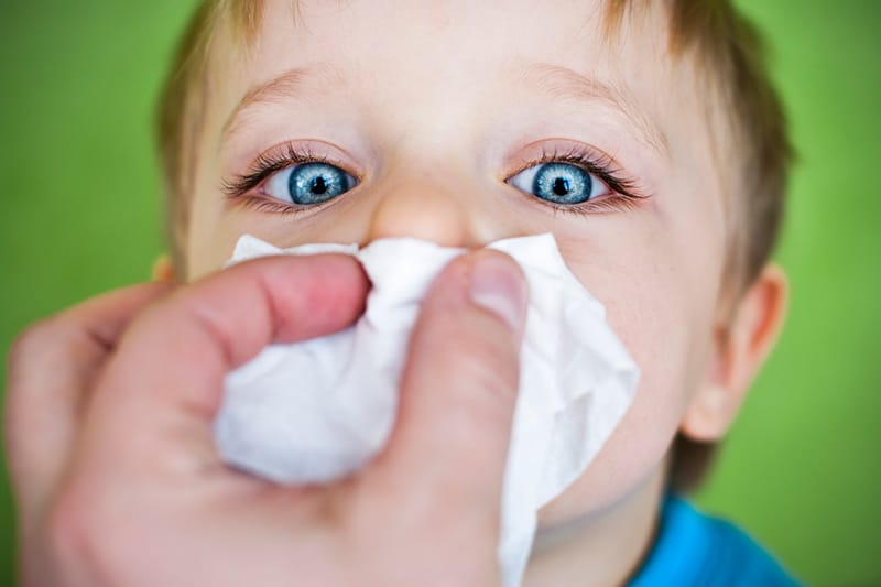 adult holding tissue up to young boys nose