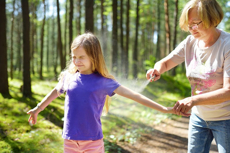 woman sprays bug spray or sunscreen onto young girl's arms