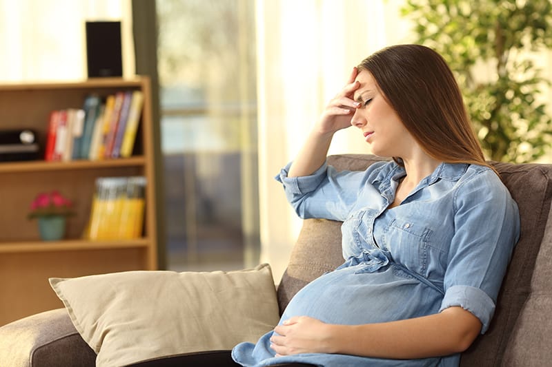pregnant woman sits on couch with hand on forehead