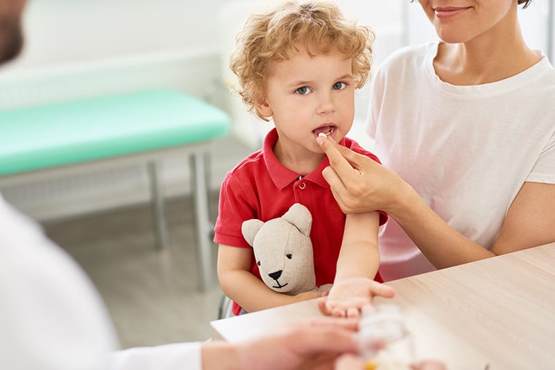 a parent feeds a little boy a kids vitamin