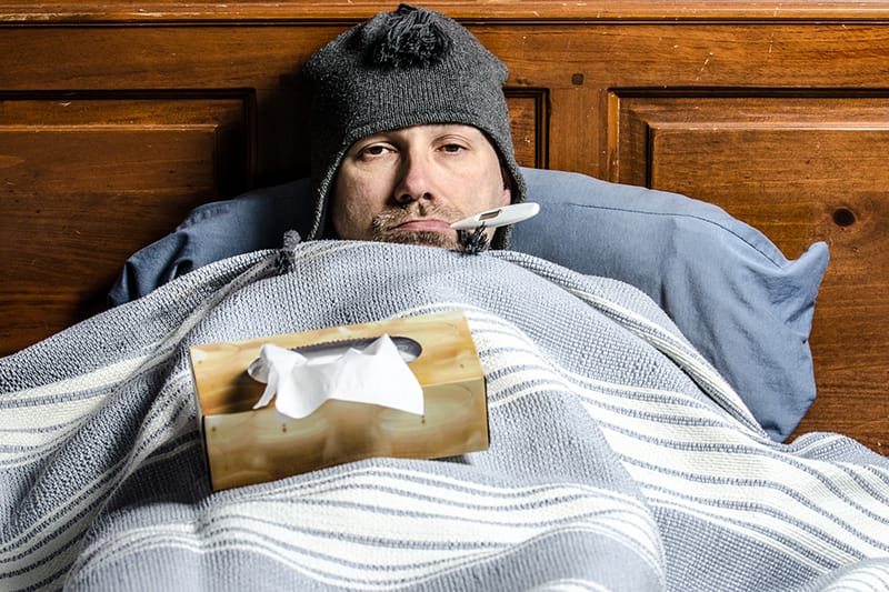 man sick in bed with a thermometer and tissues