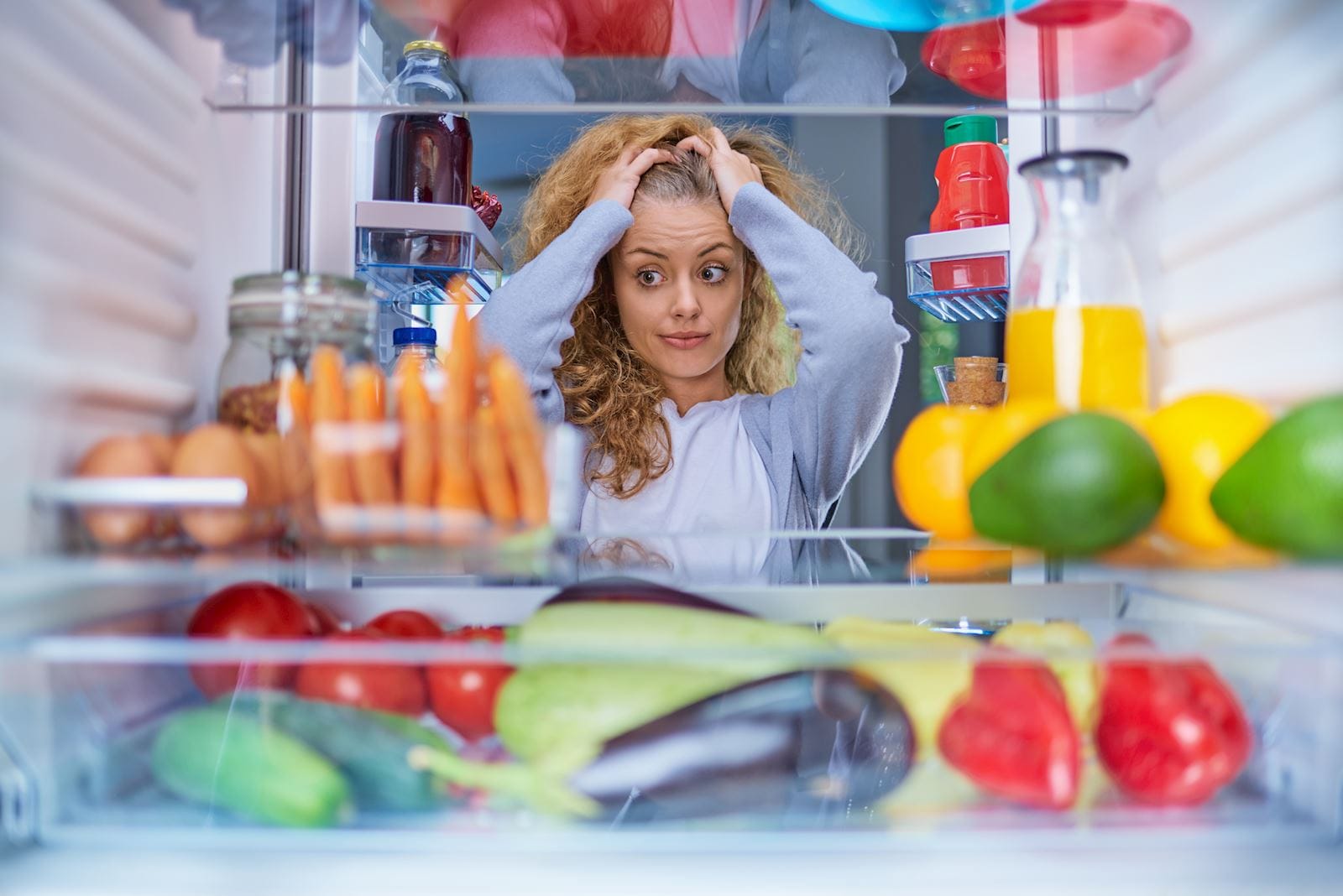 woman looks into fridge stressed with hands on her head