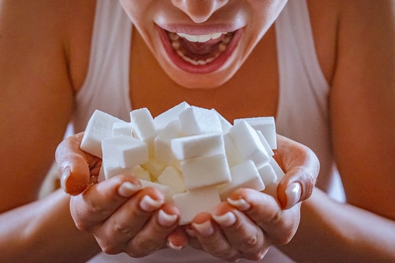 person opening mouth over large handful of sugar cubes
